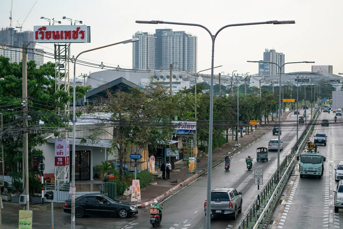 ภาพมุมสูงแสดงป้ายโลโก้ขนาดใหญ่ของร้านเรือนเพชรสุกี้ สาขาเลี่ยงเมืองนนทบุรี ตั้งตระหง่านริมถนนที่มีรถสัญจรไปมา โดยมีตัวอาคารร้าน ต้นไม้ และทัศนียภาพของตึกสูงในเมืองเป็นฉากหลัง