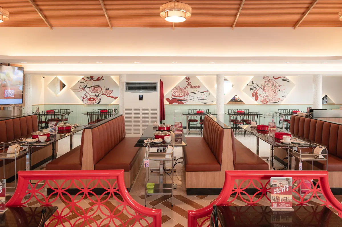 มุมมองแบบสมมาตรแสดงบรรยากาศภายในเรือนเพชรสุกี้ สาขาบางนา–ตราด 23 โดดเด่นด้วยโซนที่นั่งโซฟาหนังสีน้ำตาลแบบบูธที่นั่งสบาย เก้าอี้ฉลุลายสีแดงด้านหน้า และภาพวาดศิลปะเรื่องราวของร้านบนผนัง เป็นร้านอาหารใกล้เซ็นทรัลบางนาที่ตกแต่งอย่างสวยงามและกว้างขวาง